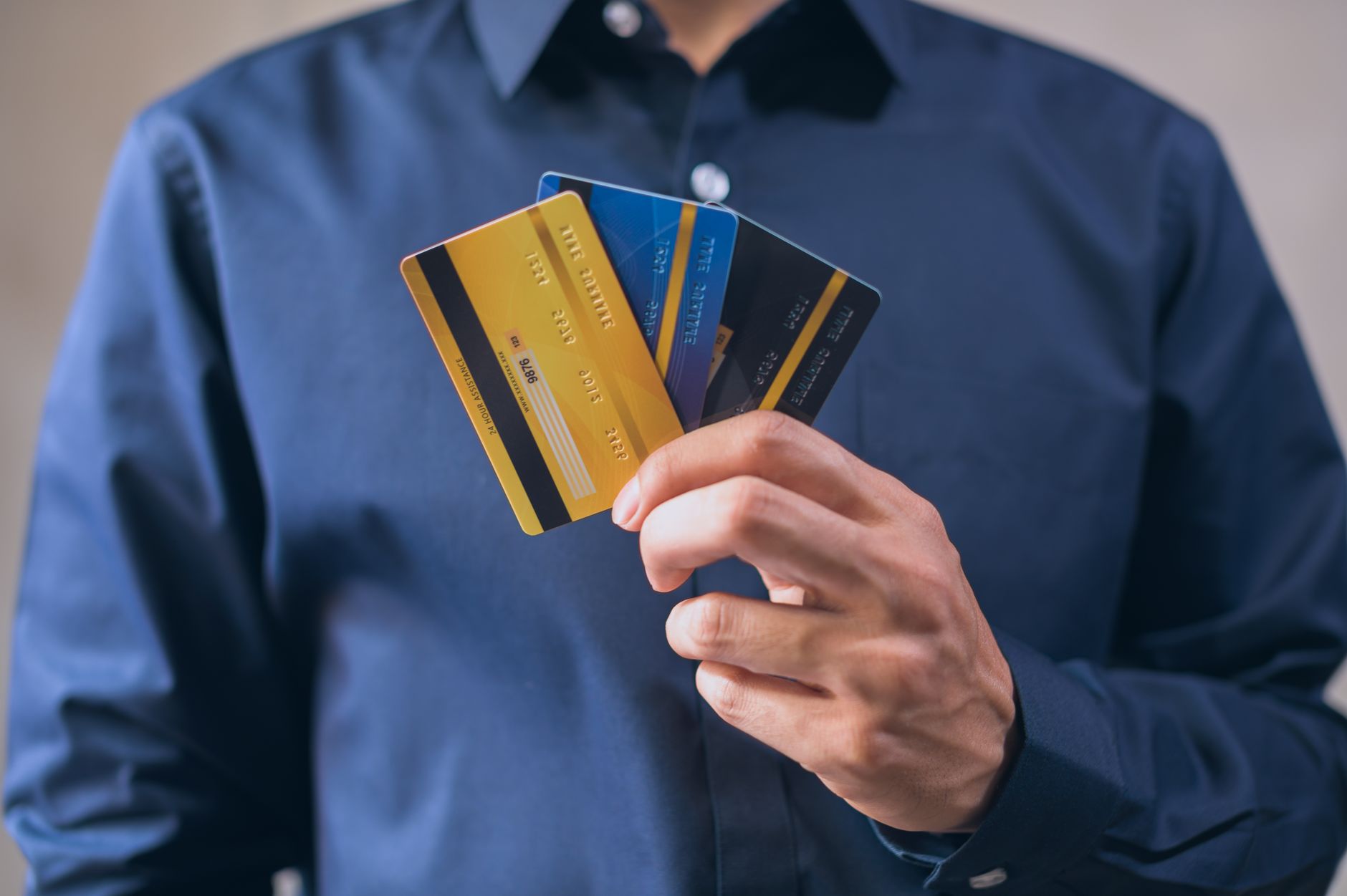 man in blue dress shirt holding three credit cards